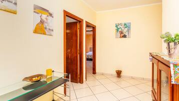 A room with a glass-top desk, a wooden door, a bed, and a painting on the wall.