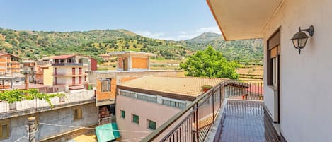 A balcony with a view of a hilly landscape, a tiled floor, and a railing.
