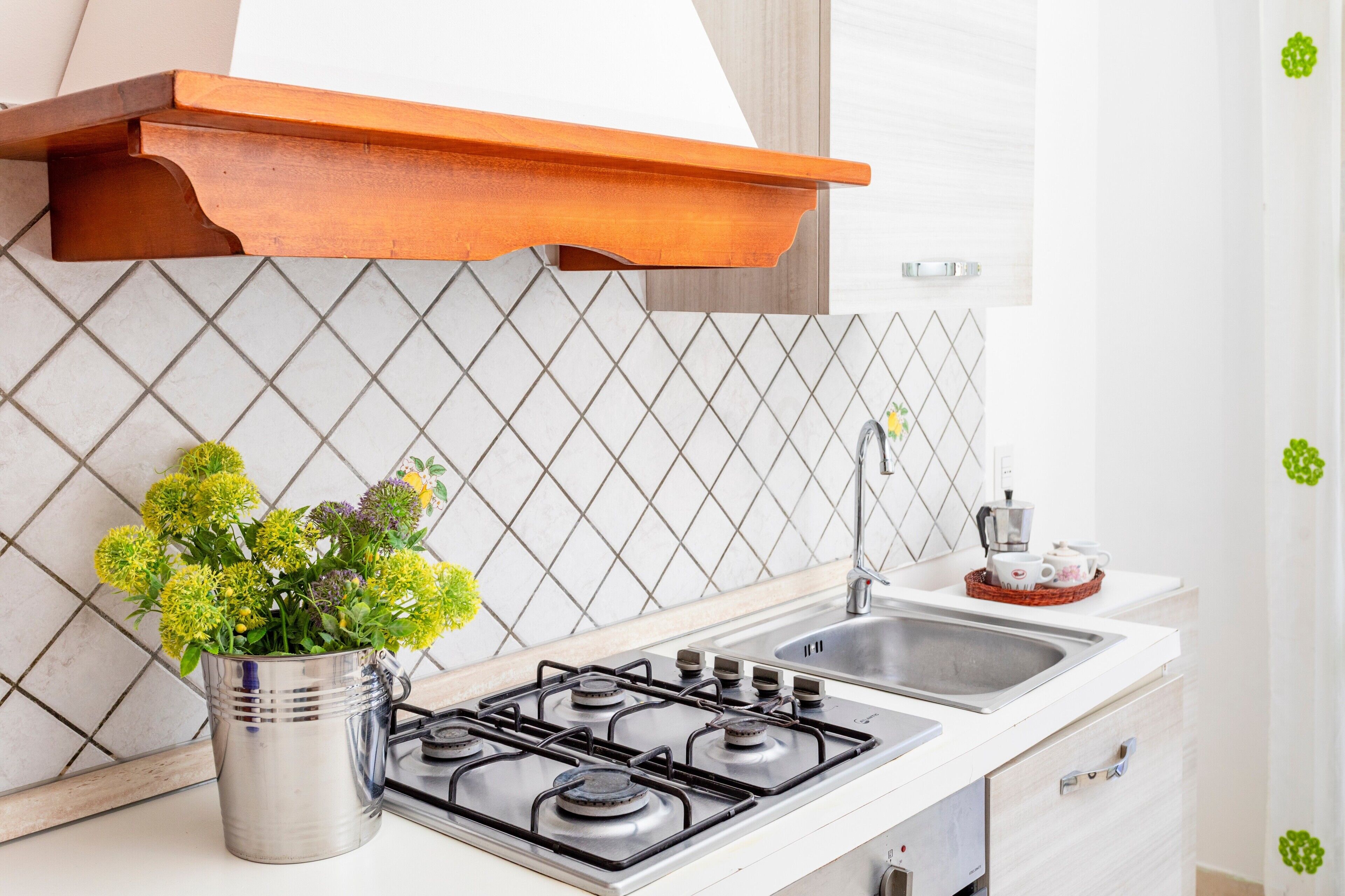 A kitchen with a gas stove, a sink, a wooden shelf, and a potted plant.