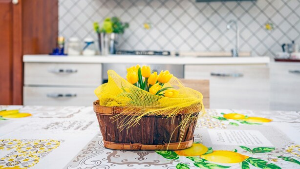 Een keuken met een houten mand met gele tulpen en een witte tafelkleed met een citroenmotief.