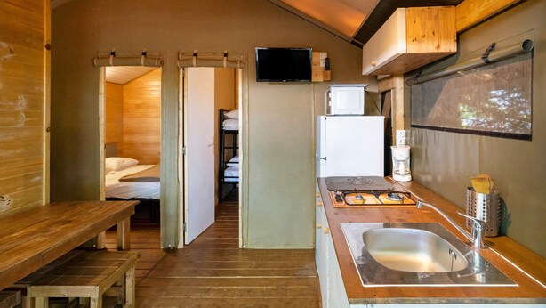 A compact room with a wooden bench, a small kitchenette with a sink, a television, and a bed in the background. - "Lodge 1" with Shared Pool, Private Terrace, and Shared Garden (Lesperon)