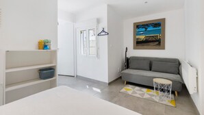 Una habitación moderna con un sofá gris, una pequeña mesa redonda, un cuadro de una playa y una puerta blanca que da a otra habitación.