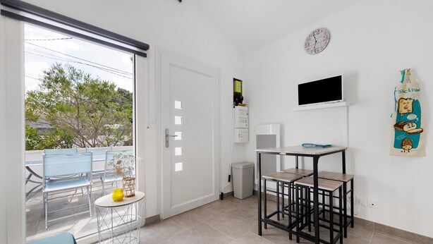 Una habitación con puerta corrediza de vidrio que da a un balcón, una mesita redonda con una silla, un televisor montado en la pared y un reloj de pared.