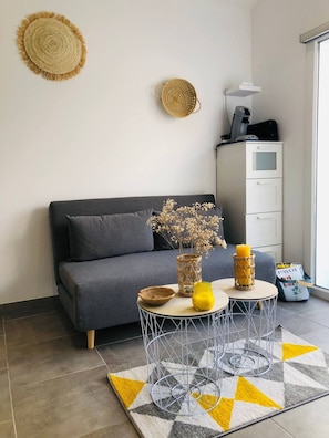 Un salon moderne avec un canapé gris, une table basse ronde sur laquelle est posée une bougie jaune, et un tapis à motifs.