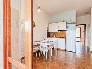 Une cuisine compacte avec des meubles blancs, une table à manger avec des chaises, un luminaire suspendu et un réfrigérateur.