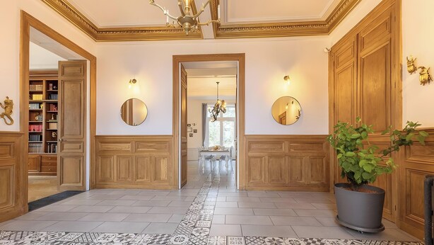 A hallway with wooden paneling, a potted plant, and a chandelier.