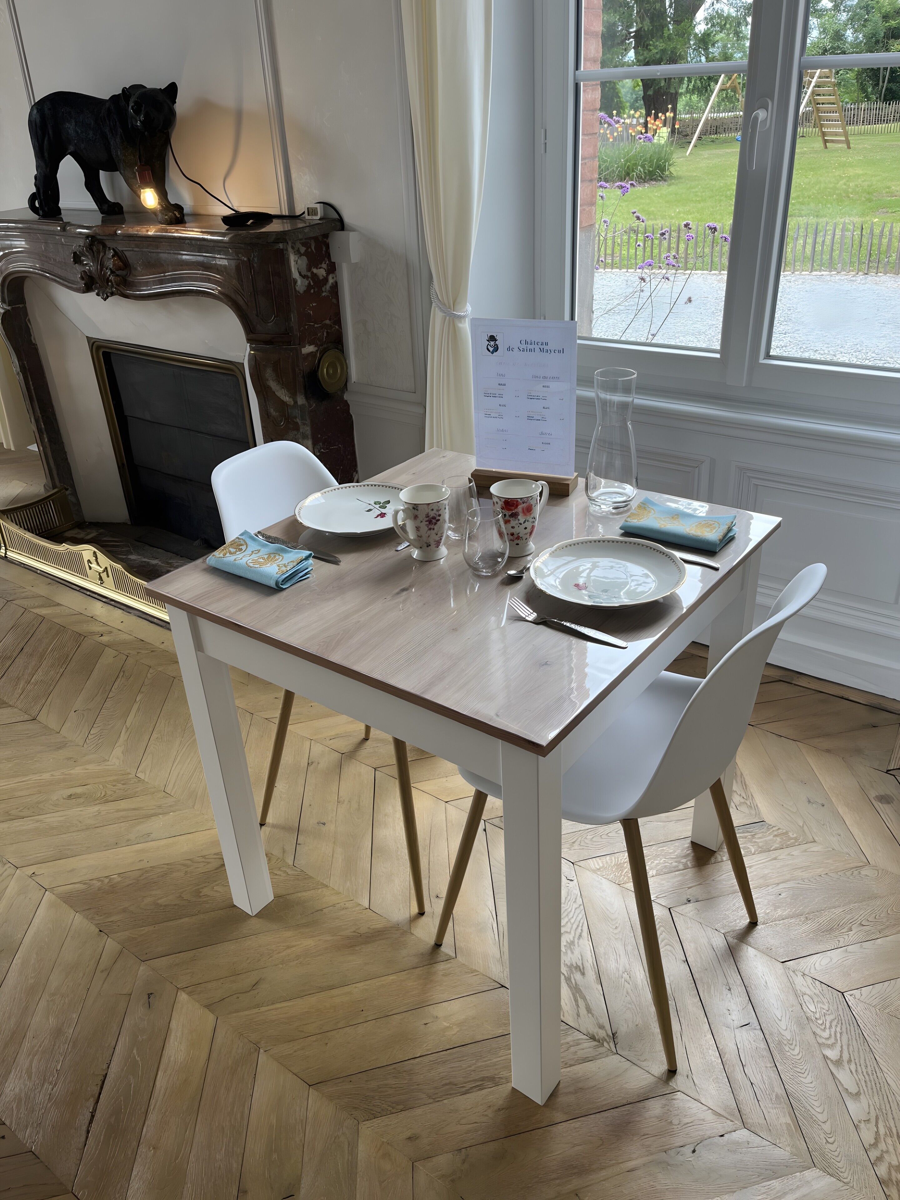 A dining table with chairs, a menu stand, and a fireplace with a decorative dog figurine.