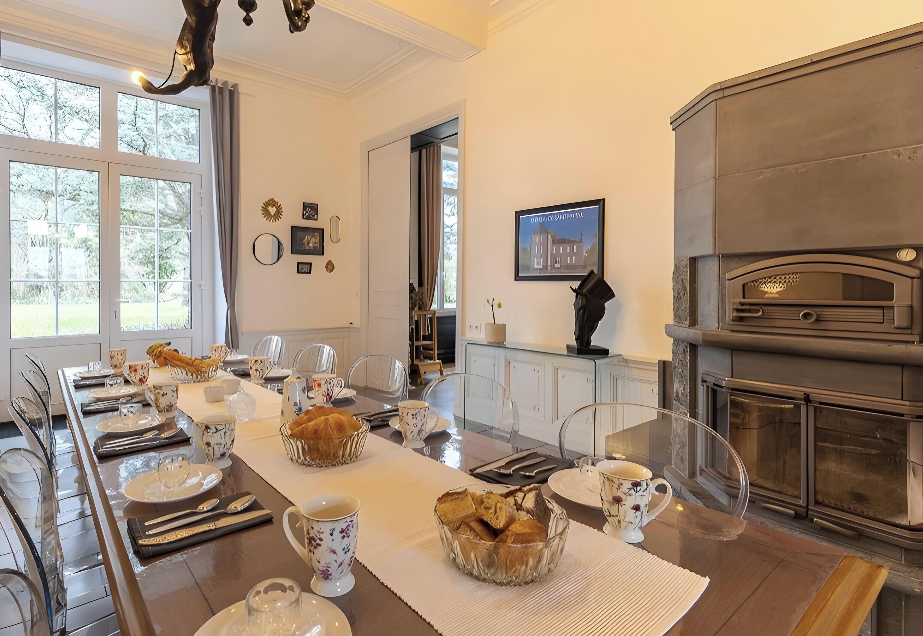 A dining room with a long table set for a meal, a fireplace, and a view of the outdoors.