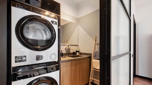A compact laundry area with a front-loading washer and dryer, a small sink, and a wooden cabinet.