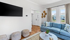 A living room with a blue sofa, ottomans, a round coffee table, and a flat-screen TV mounted on the wall.