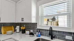 A modern kitchen with white cabinets, a granite countertop, a stainless steel sink, and a window with blinds.