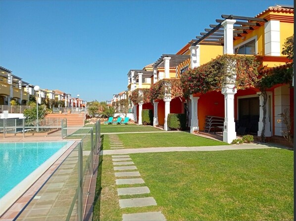 A resort with a swimming pool, a well-maintained lawn, and a row of colorful buildings with outdoor seating.