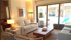 Un salon moderne comprenant un canapé, deux fauteuils, une table basse et une lampe. Une grande fenêtre offre une vue sur l’extérieur.