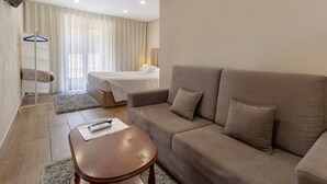 Ein Hotelzimmer mit einer Couch, einem kleinen Tisch, einem Bett, einem Fernseher und einem Fenster mit Vorhängen.