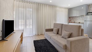 A modern living room with a sofa, a flat-screen TV, and a kitchen area in the background. - Apartment 'E' with Mountain View, Wi-Fi and Air Conditioning (Geres)