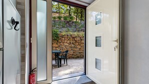 A room with a stone wall, a fire extinguisher, and a door leading to an outdoor area with a table and chairs. - Apartment 'E' with Mountain View, Wi-Fi and Air Conditioning (Geres)