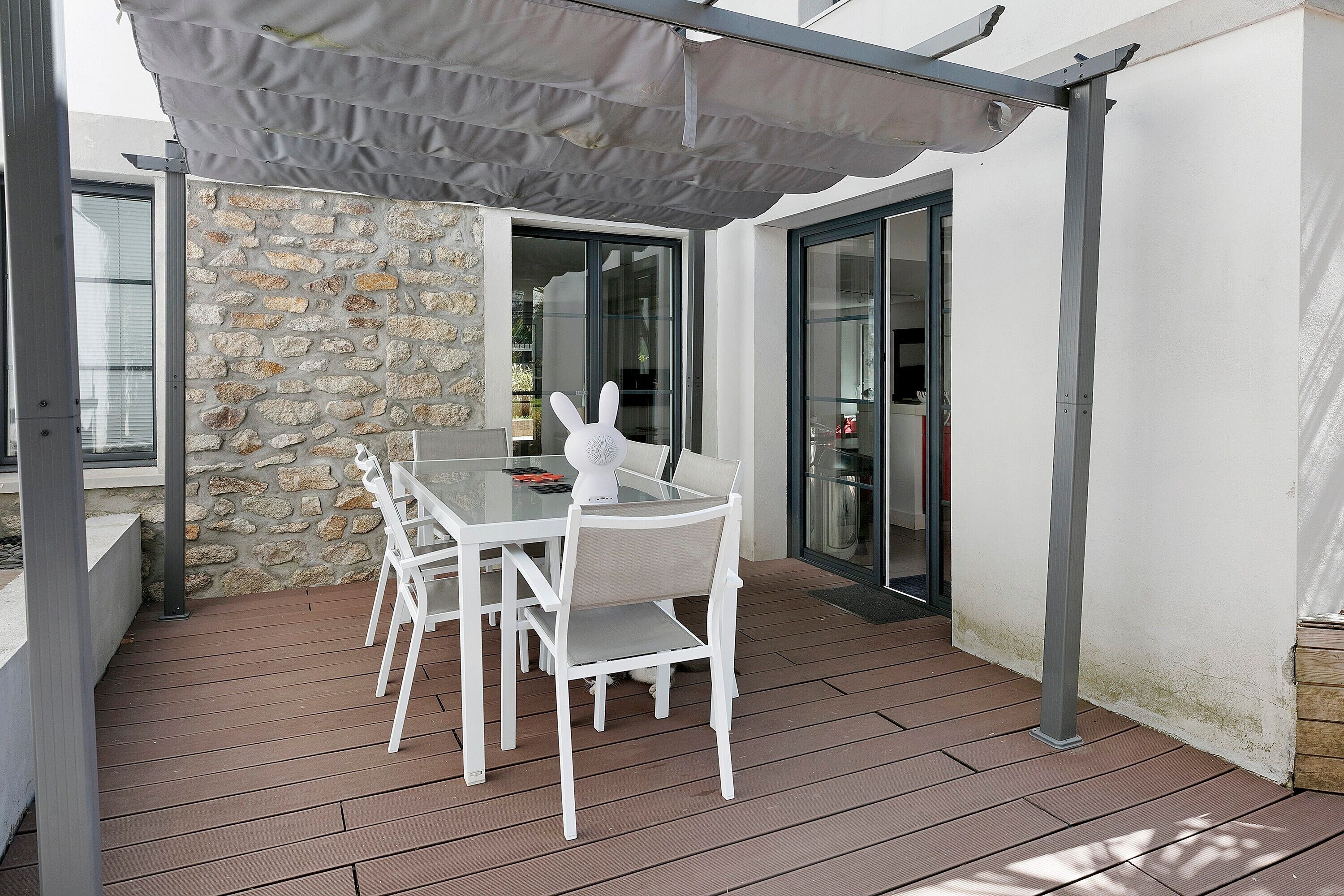 A covered patio area with a table and chairs, a stone wall, and a glass door leading to an interior space.