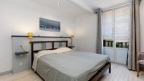 Ein Schlafzimmer mit einem Bett, Nachttischlampen, einem Gemälde und einem Fenster mit Vorhängen.