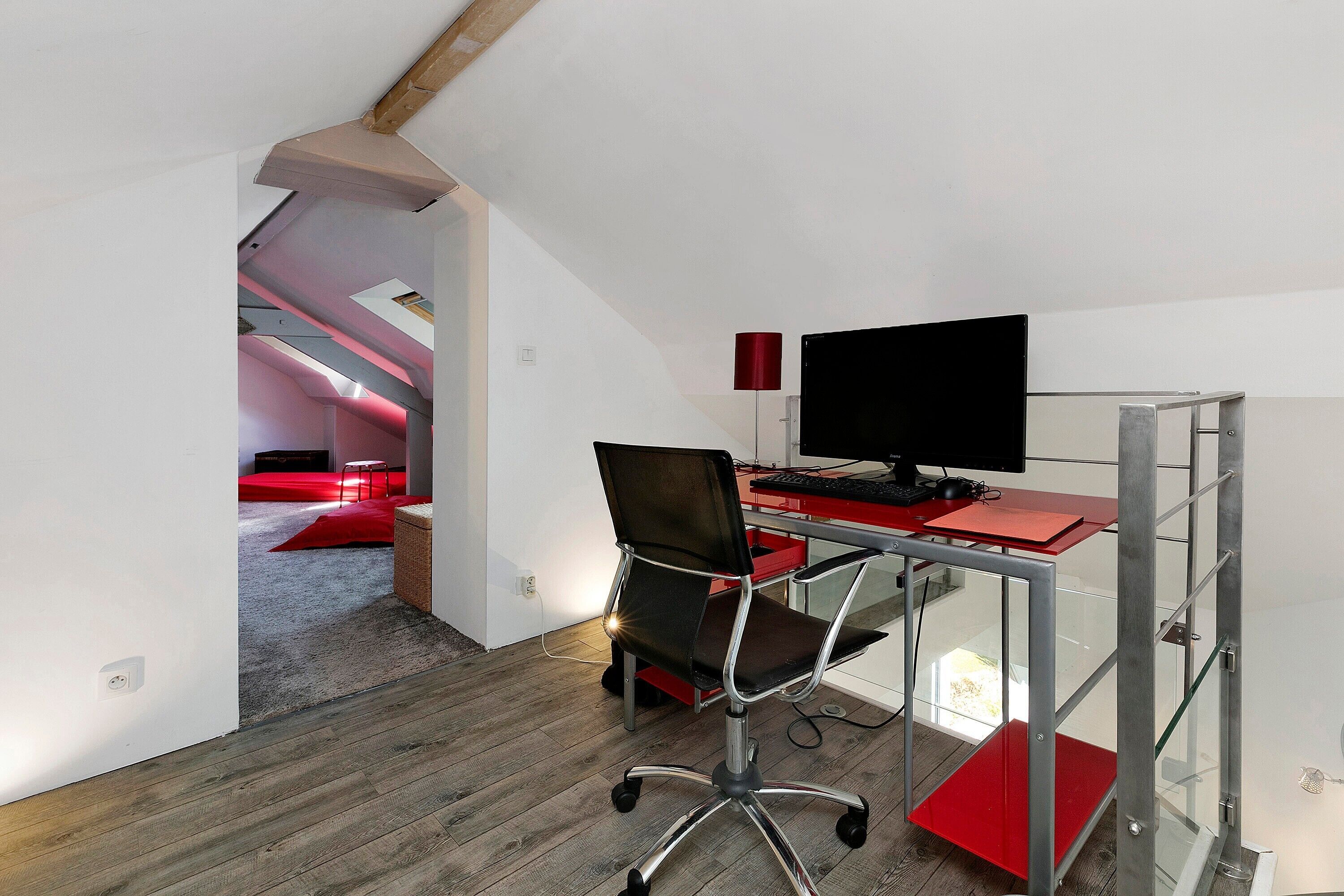 Ein moderner Büroraum mit Schreibtisch, Stuhl, Computer und einer roten Akzentwand.