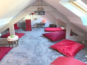 A cozy attic bedroom with a sloped ceiling, red cushions, a small round table, and a lamp.