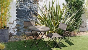 Ein Gartenbereich mit einer Steinsäule, zwei Korbstühlen und einem kleinen runden Tisch.