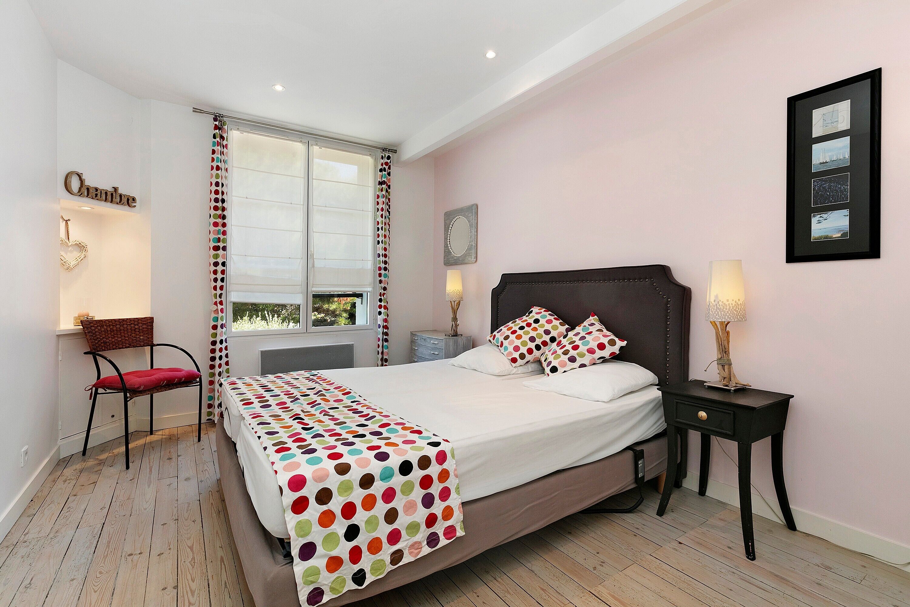 Een slaapkamer met een bed, een stoel, een nachtkastje, een lamp en een raam.