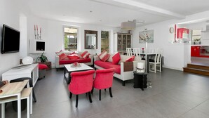 Ein modernes Wohnzimmer mit Sofa, Sesseln, einem Esstisch und einer Küchenzeile.