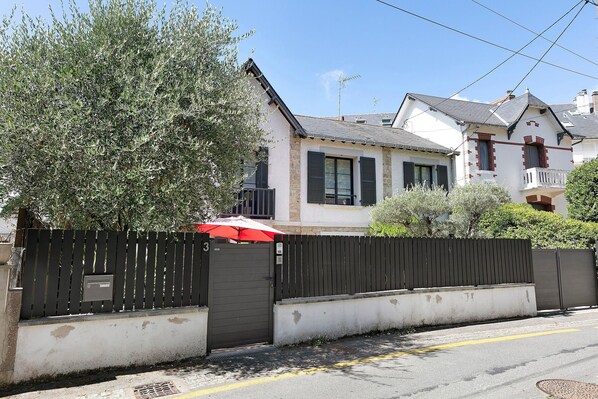 Propiedad residencial con entrada vigilada, una sombrilla roja y un edificio blanco de fachada de piedra.