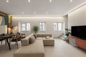 A modern living room with a sectional sofa, a dining table with chairs, a flat-screen TV, and a staircase leading to an upper level. - The Great Rose Retreat (Nazaré)