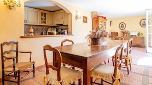 Zona pranzo con tavolo e sedie in legno, una cucina sullo sfondo e un centrotavola decorativo con una pianta.