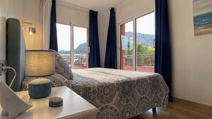 A hotel room with a bed, a desk with a lamp, a small ottoman, and a window with curtains. - Apartment with terrace and pool in L'Estartit. (Torroella de Montgrí)