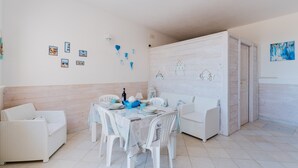 Un comedor con una mesa dispuesta para cuatro personas, mobiliario de mimbre blanco y adornos en la pared.