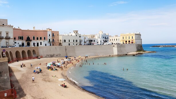 Un pueblo costero con una playa de arena, un muro marítimo y edificios coloridos.