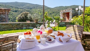 Una mesa servida con alimentos para el desayuno, un muro de piedra y vistas a colinas verdes.
