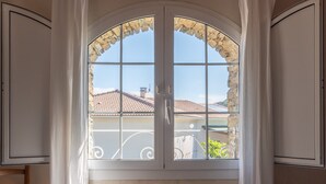 Una habitación con un amplio ventanal de arco, cortinas blancas y vistas a un edificio con tejado de azulejos.