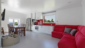 Una cocina moderna con armarios blancos, un sofá rojo y una zona de comedor con mobiliario de madera.