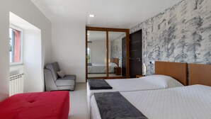 Una habitación de hotel con dos camas, un sofá rojo, un sillón gris, un armario de madera y una pared con estampado de mármol.