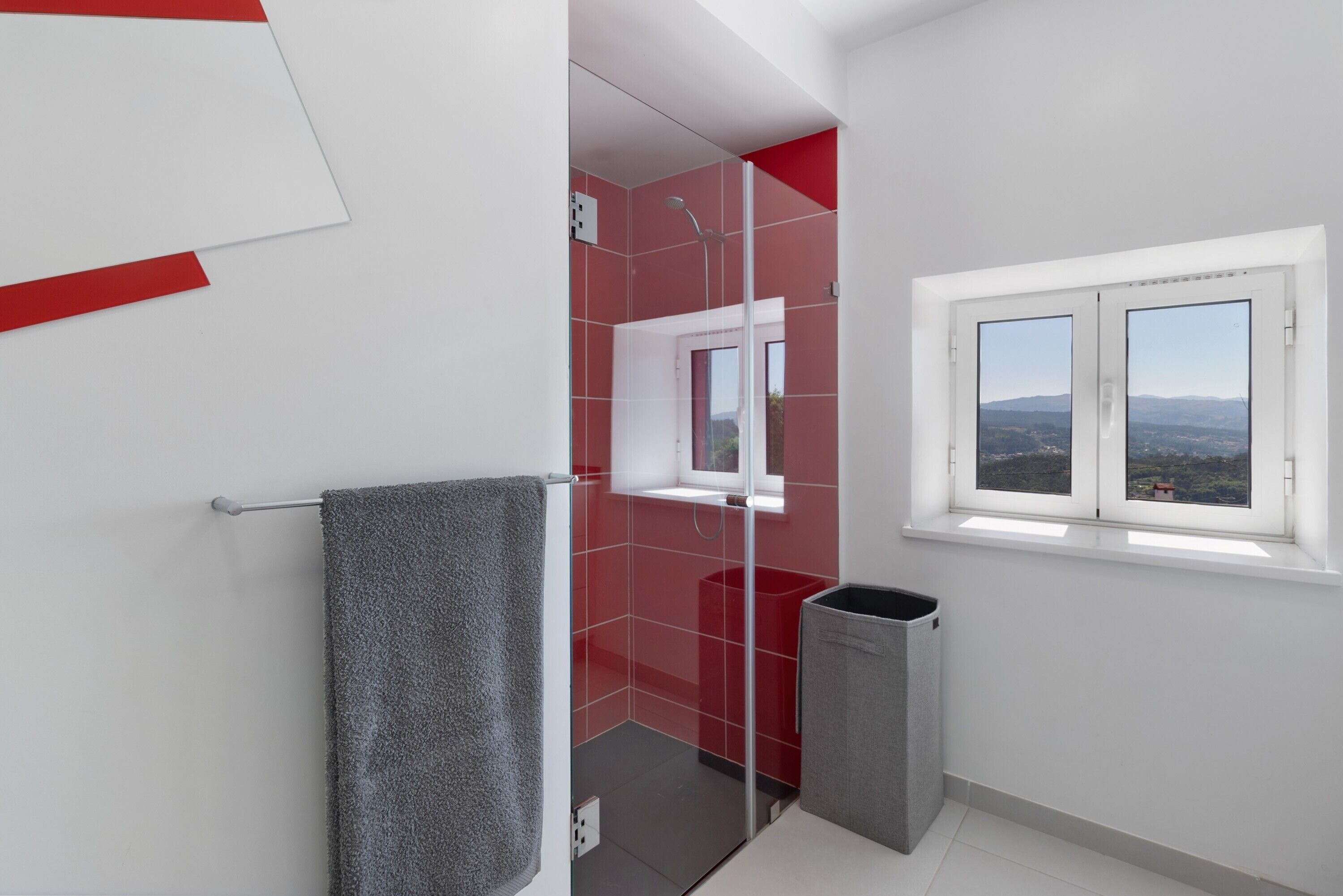 Un baño con ducha, una ventana con vistas, un perchero para toallas y un cubo de basura.