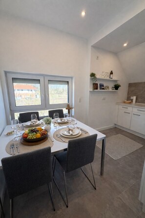 A dining area with a table set for four, a bowl of fruit, and a view of the outside.