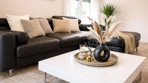 Ein modernes Wohnzimmer mit einer schwarzen Ledersofa, einem weißen Couchtisch und dekorativen Elementen, darunter eine Vase mit Pampasgras.