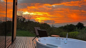 Una terraza de madera con un jacuzzi, una puerta de vidrio y vistas a un paisaje al atardecer.