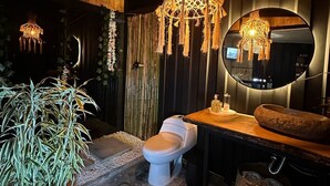 Un baño moderno con inodoro blanco, tocador de madera, un espejo grande y una lámpara de araña colgante.