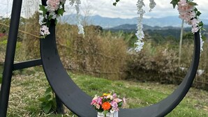 Marco negro circular con un arreglo floral colgante y un pequeño ramo sobre un pedestal.