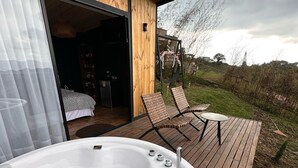 Un jacuzzi con pétalos de flores, una terraza de madera y un dormitorio con cama y armario.