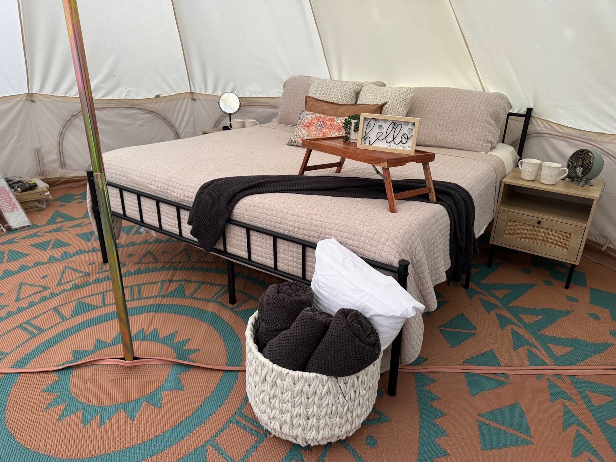 A tented accommodation with a bed, a bedside table with a fan, and a decorative sign.