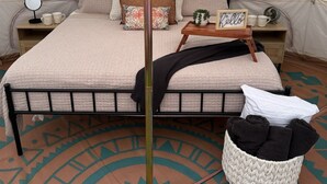Habitación tipo alojamiento en tienda con cama, mesita de noche y un taburete de madera.