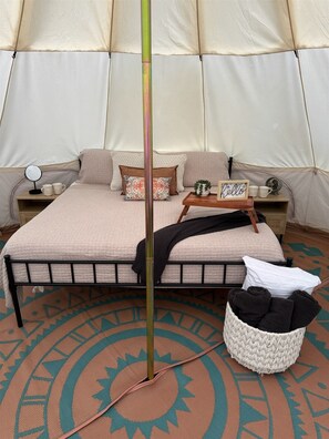 Habitación tipo alojamiento en tienda con cama, mesita de noche y un taburete de madera.
