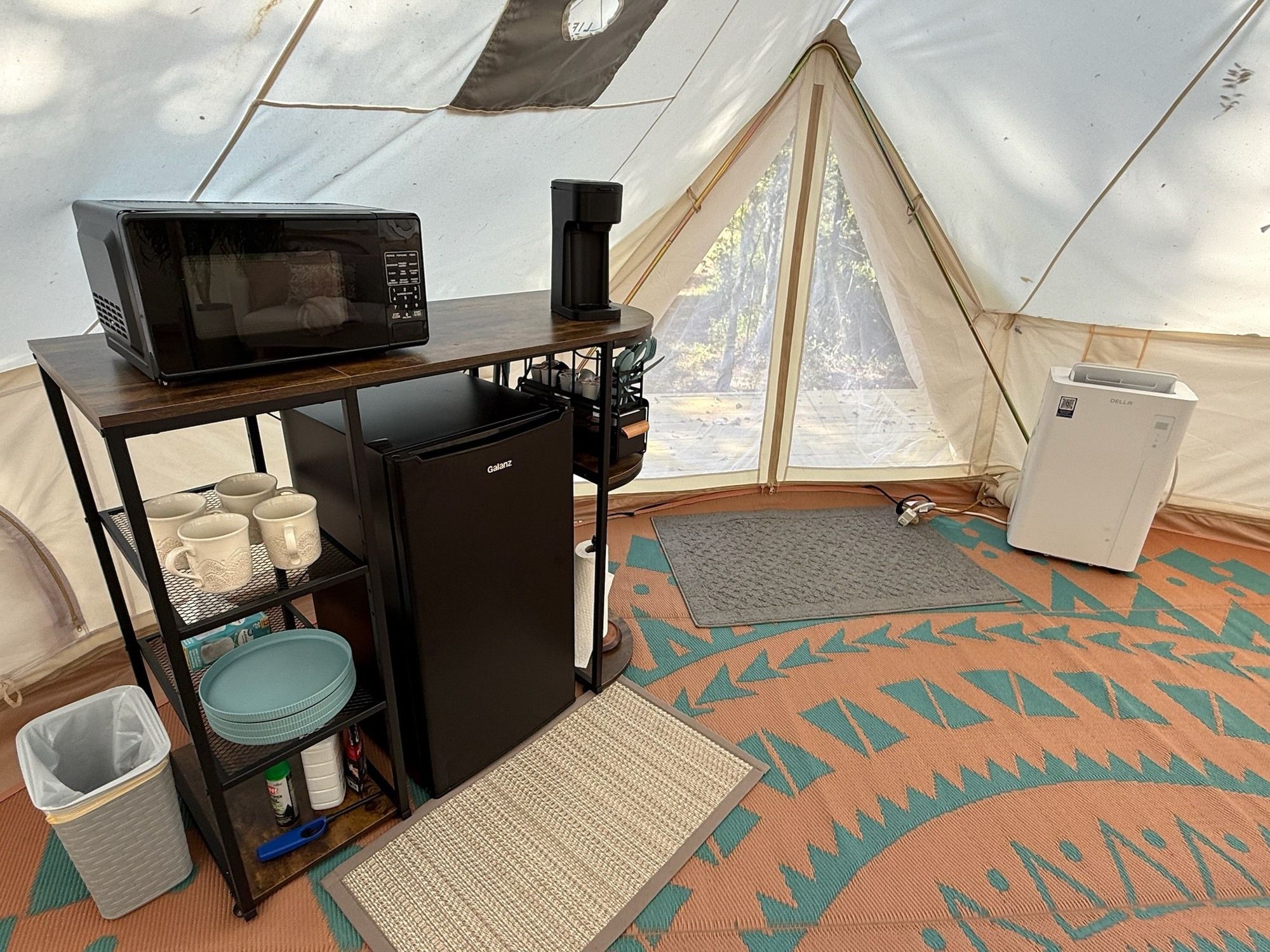 A compact kitchenette with a microwave, refrigerator, and coffee maker inside a tent.