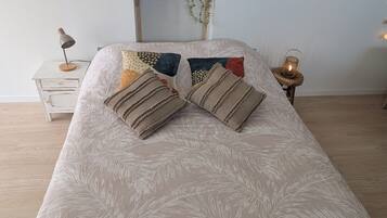 A neatly arranged bedroom with a bed, bedside tables, a shelf with decorative items, and a mirror with lights.