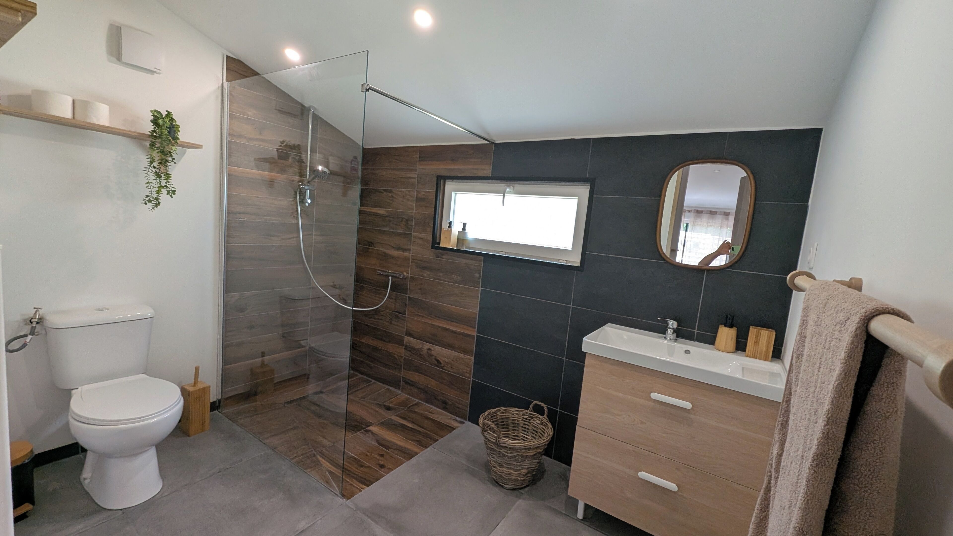 A modern bathroom with a glass-enclosed shower, a white toilet, a wooden vanity, and a mirror.